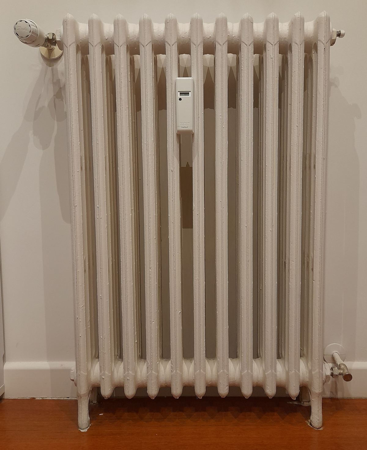 Radiateur à eau blanc équipé d’un robinet thermostatique et d’un répartiteur de frais de chauffage
