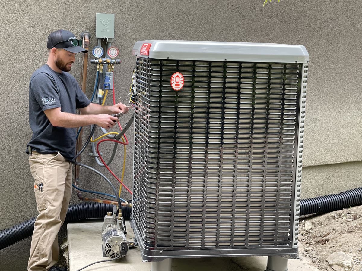 Technicien intervenant sur une pompe à chaleur extérieure avec des manomètres et des flexibles